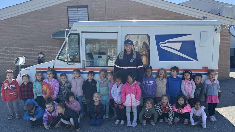 A local mail carrier visiting the classroom with a USPS truck as part of Community Workers Week