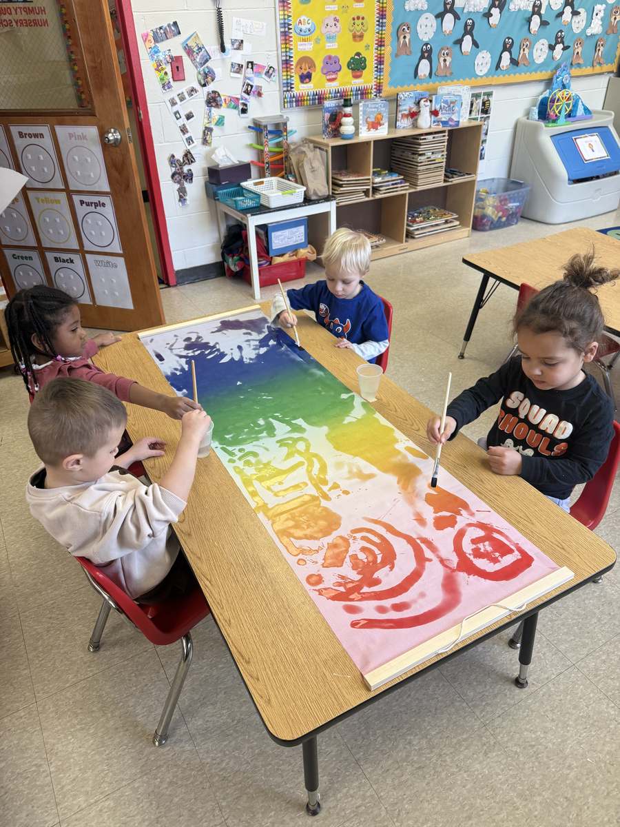 Preschoolers painting a rainbow watercolor artwork together