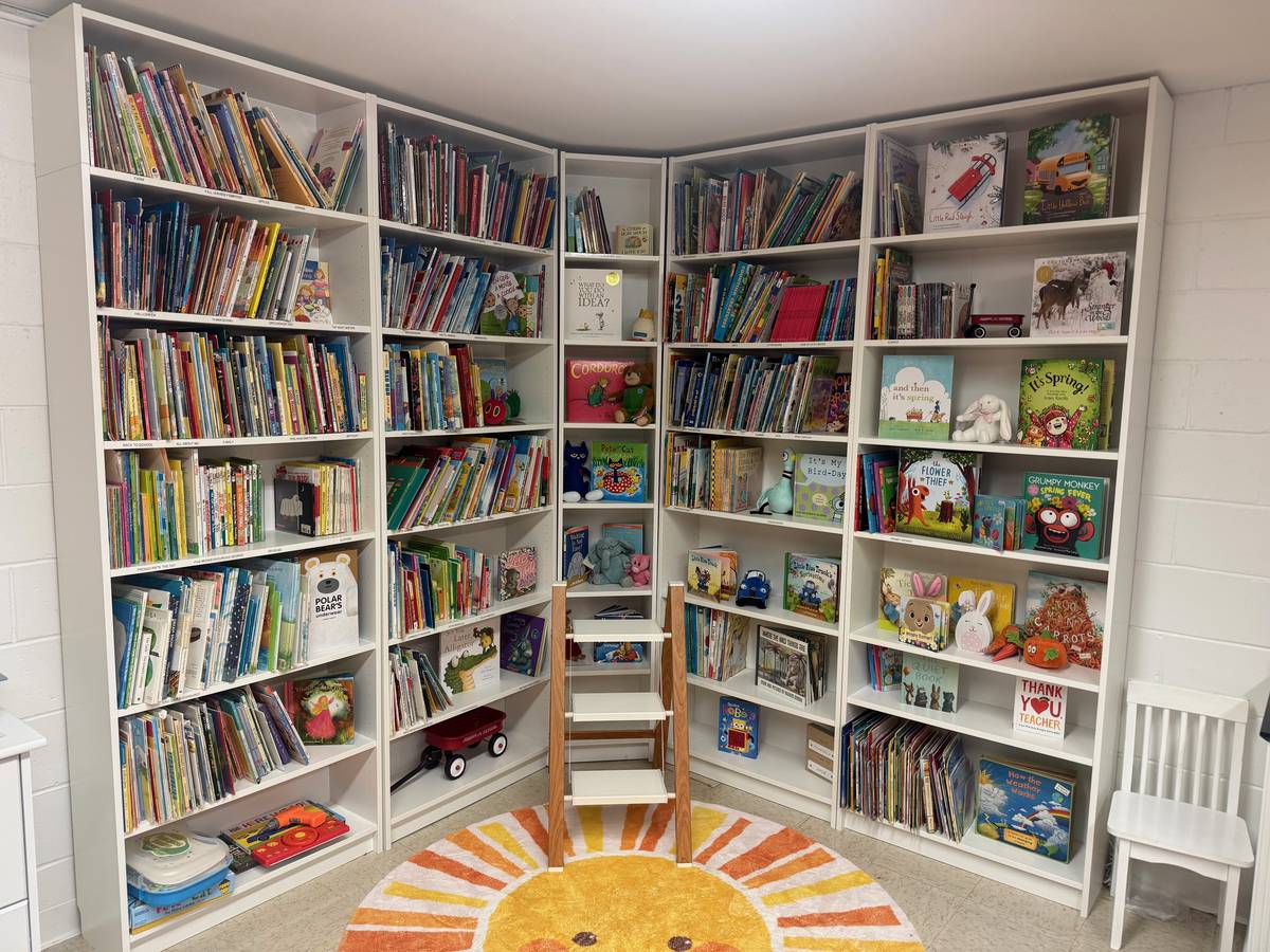 A cozy classroom library corner with a sun-shaped rug and shelves of books